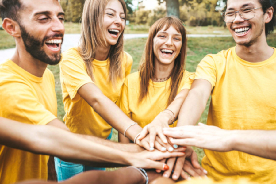 Gruppe in gelben T-Shirts legt Hände übereinander und lacht.