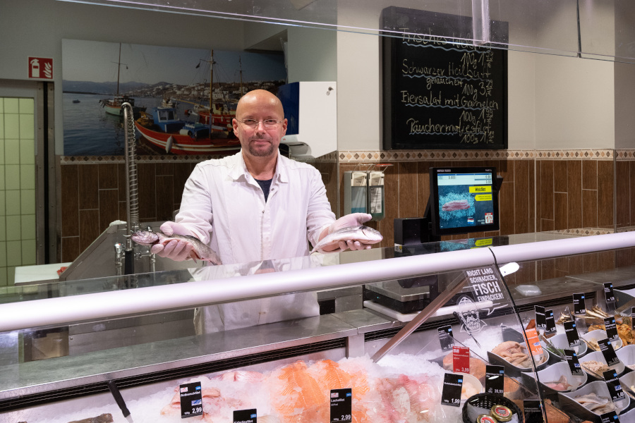Fischhändler hinter der Theke hält zwei frische Fische in den Händen.