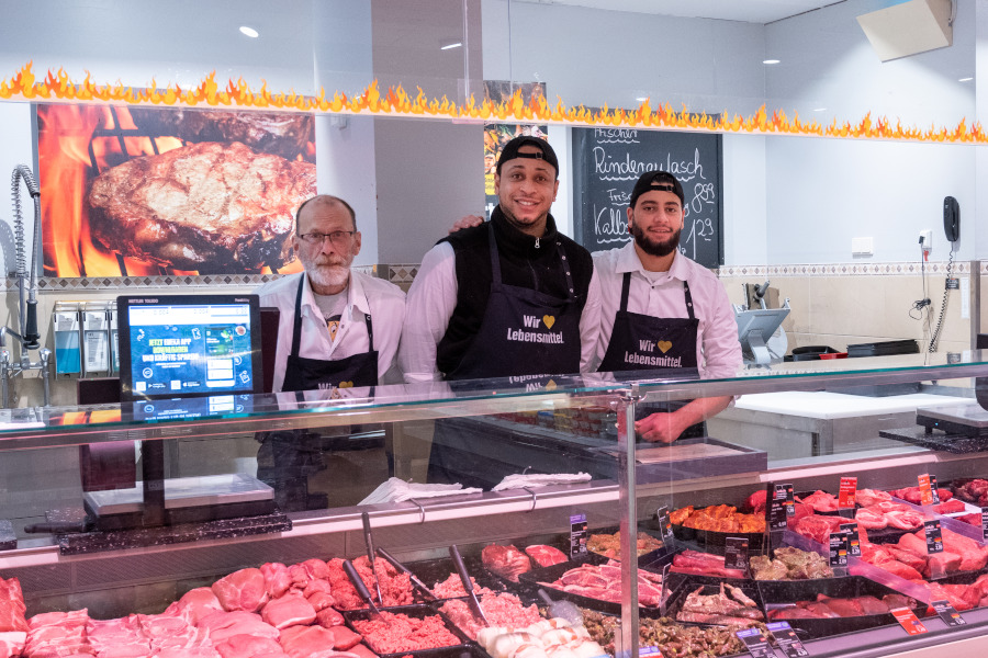Drei Mitarbeitende an der Metzgereitheke vor Fleisch- und Wurstwaren.